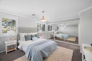 A bedroom with a large bed, a bedside table, a mirror, and a window with blinds.