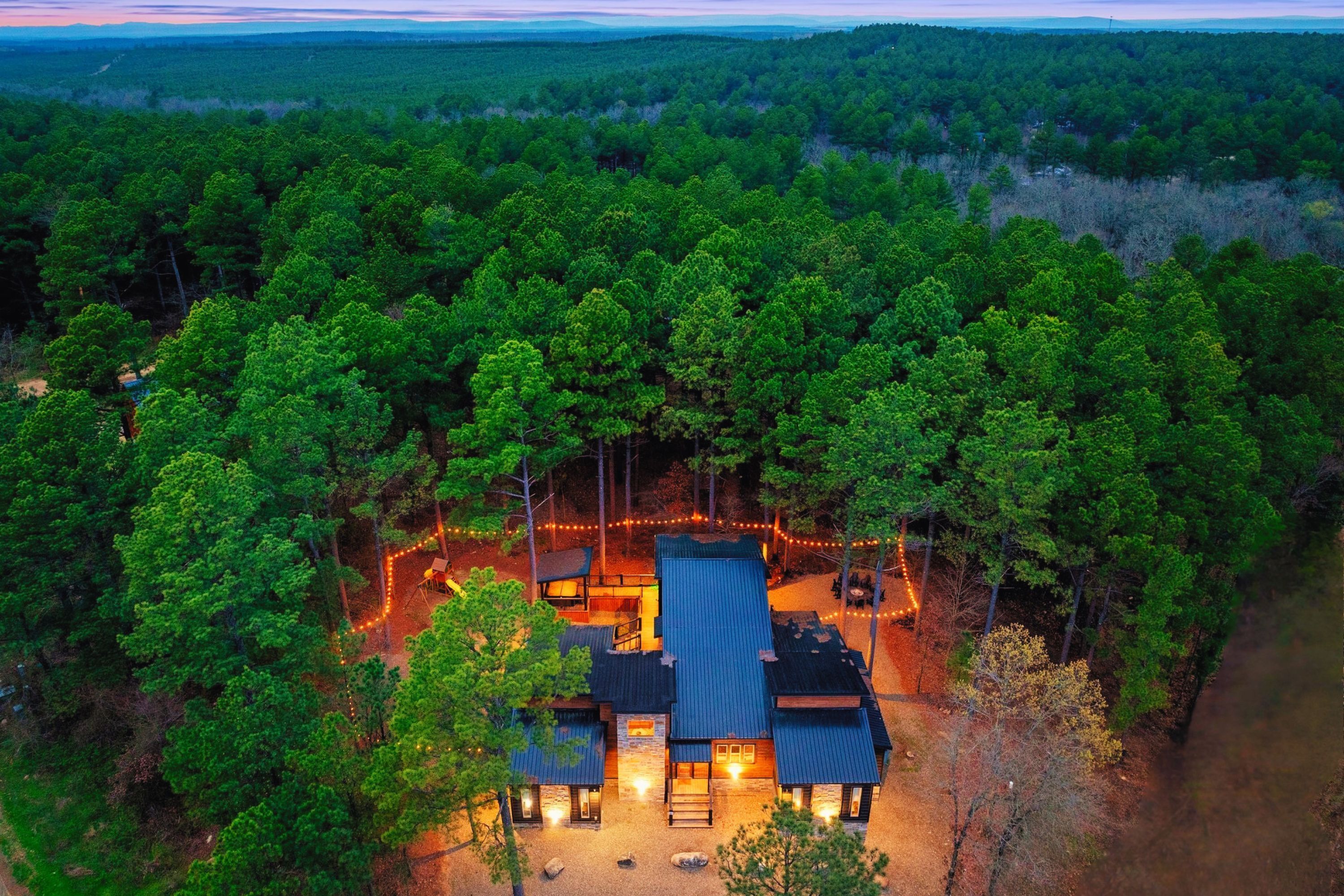 Un chalet à étages, entouré d’une forêt dense, doté d’un patio bien éclairé et de plusieurs entrées.