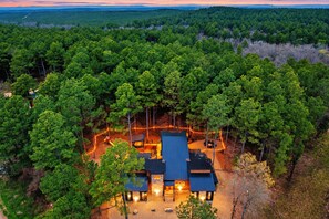 A lodge surrounded by dense forest, with a main building and smaller structures, accessible by a dirt path.