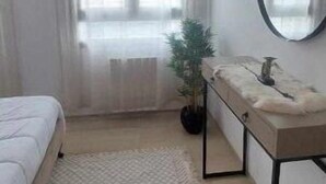 Een slaapkamer met een bed, nachtkastje, spiegel, raam met gordijnen en een kamerplant.