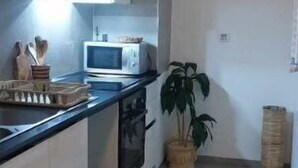 Een moderne keuken met witte kasten, een zwart aanrecht, een magnetron en een fornuis. Op de vloer ligt een zwart vloerkleed en in de hoek staat een potplant.