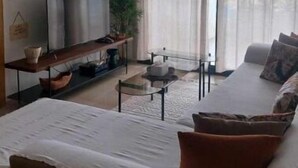 Een moderne woonkamer met een bank, een televisie, een salontafel en een groot raam met gordijnen.