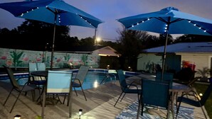 An outdoor pool area with blue umbrellas, poolside chairs, and a decorative tile wall. - Mermaid Dreams: Spacious 3 bedrooms 2.5 bath with pool ALL in golf cart district (Ocean Springs)