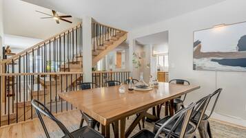 Uma sala de jantar espaçosa com mesa e cadeiras de madeira, escada com corrimão de madeira e um ventilador de teto moderno.