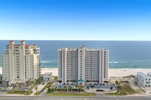 A high-rise hotel with multiple balconies, a beach view, and a parking area.