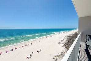 A beach view from a balcony with a clear sky, a sandy beach, and umbrellas.