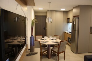 A modern kitchen with a built-in refrigerator, a dining table set for four, and a vase with plants. - Aptos Noroeste by CentoEdez (Brasília)