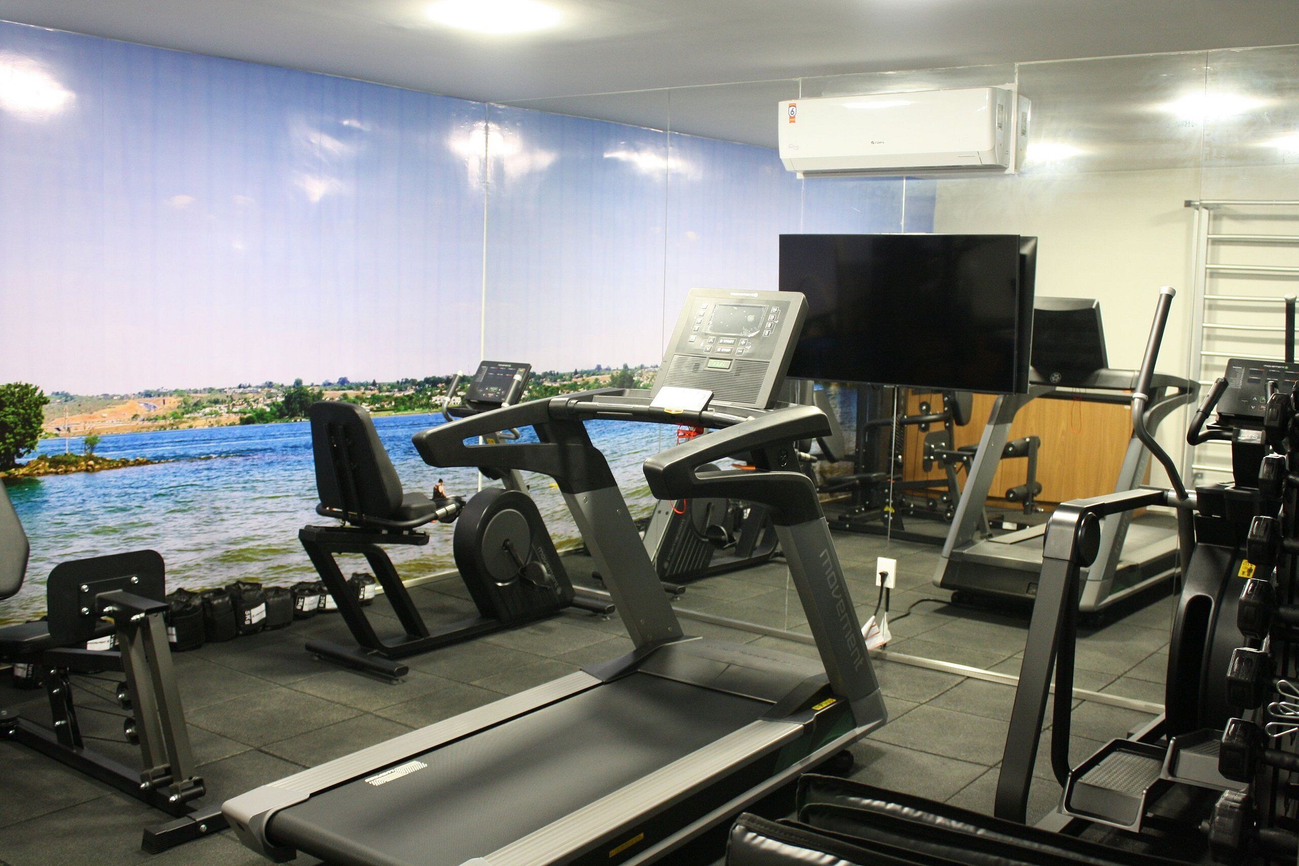 A gym with treadmills, weight machines, and a large TV screen.