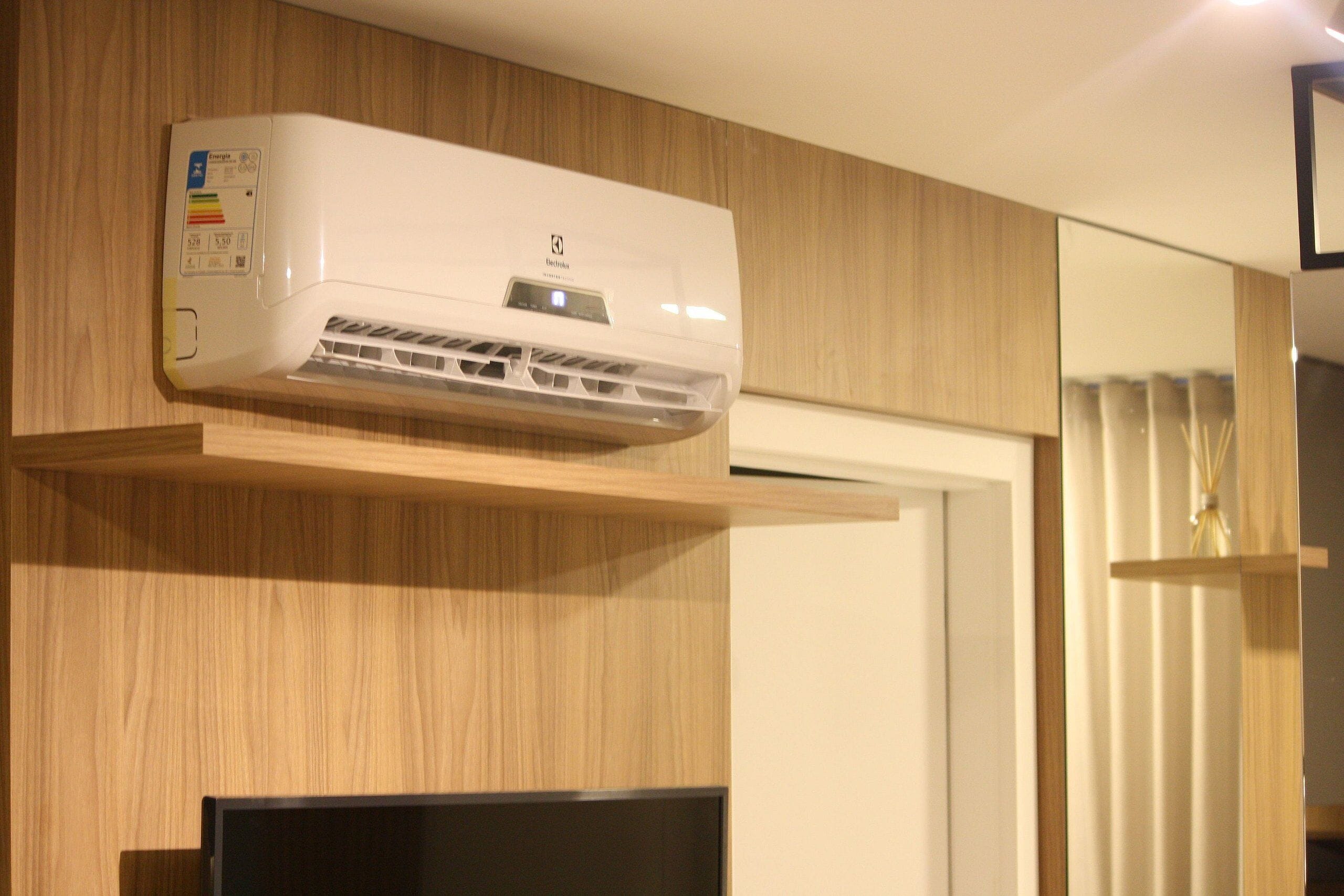 A white air conditioning unit mounted on a wooden wall with a built-in television below it.