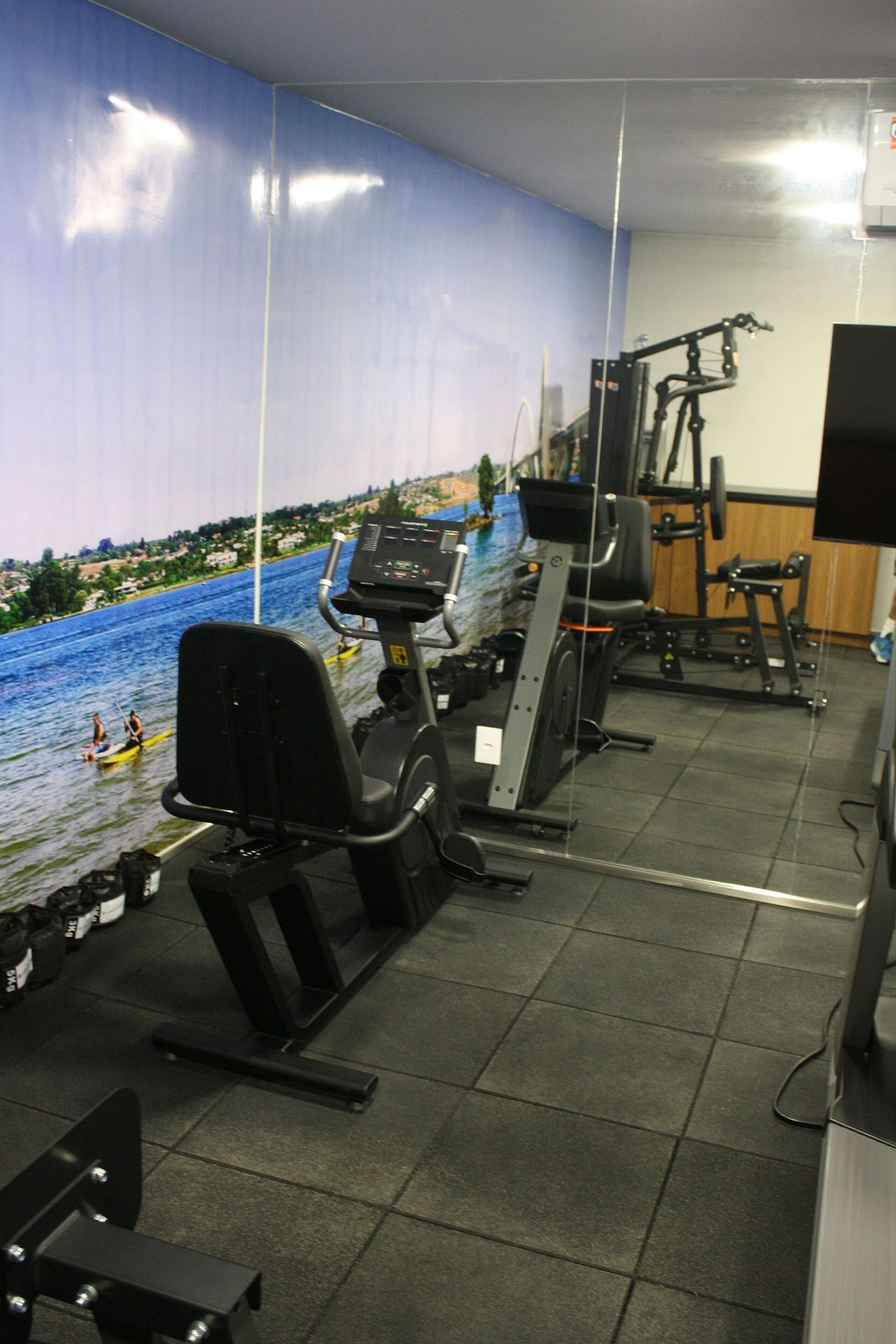 A gym with exercise equipment, a large mural of a river scene, and a television screen.