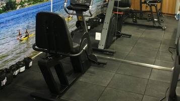 A gym with exercise equipment, a large mural of a river scene, and a television screen.