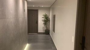 Un couloir moderne au design long et étroit, agrémenté de spots encastrés au plafond, d’une plante en pot et d’une porte au bout.