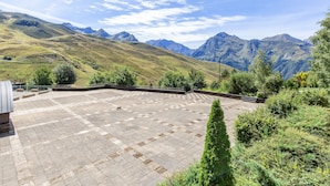 A courtyard with a tiled floor, surrounded by greenery and mountains in the background.
