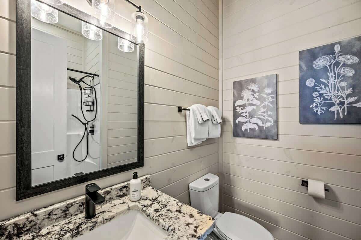 Une salle de bain dotée d’un grand miroir, d’une douche, de toilettes et d’un lavabo avec un plan de travail en marbre.