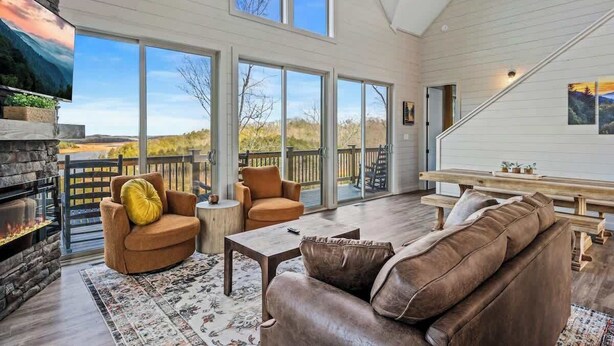 A spacious living room with a fireplace, large windows, and a deck. - NEW LAKE CABIN Sleeps 14 Indoor Pool Hot Tub (Sevierville)