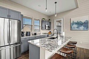 A modern kitchen with a stainless steel refrigerator, a marble island, and bar stools.