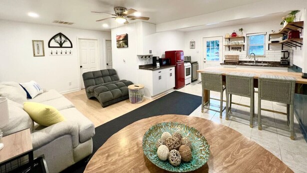 A modern living room with a sofa, a dining table with chairs, a kitchen area with a refrigerator and microwave, and a ceiling fan. - Lake Life Lodge Cottage by Belton Lake (Belton)