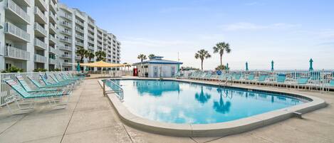 A swimming pool with lounge chairs, a lifeguard tower, and a building with balconies.