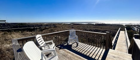 A wooden deck with white chairs overlooking a beach.