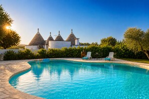 A swimming pool with lounge chairs, a stone wall, and a building with conical roofs in the background.
