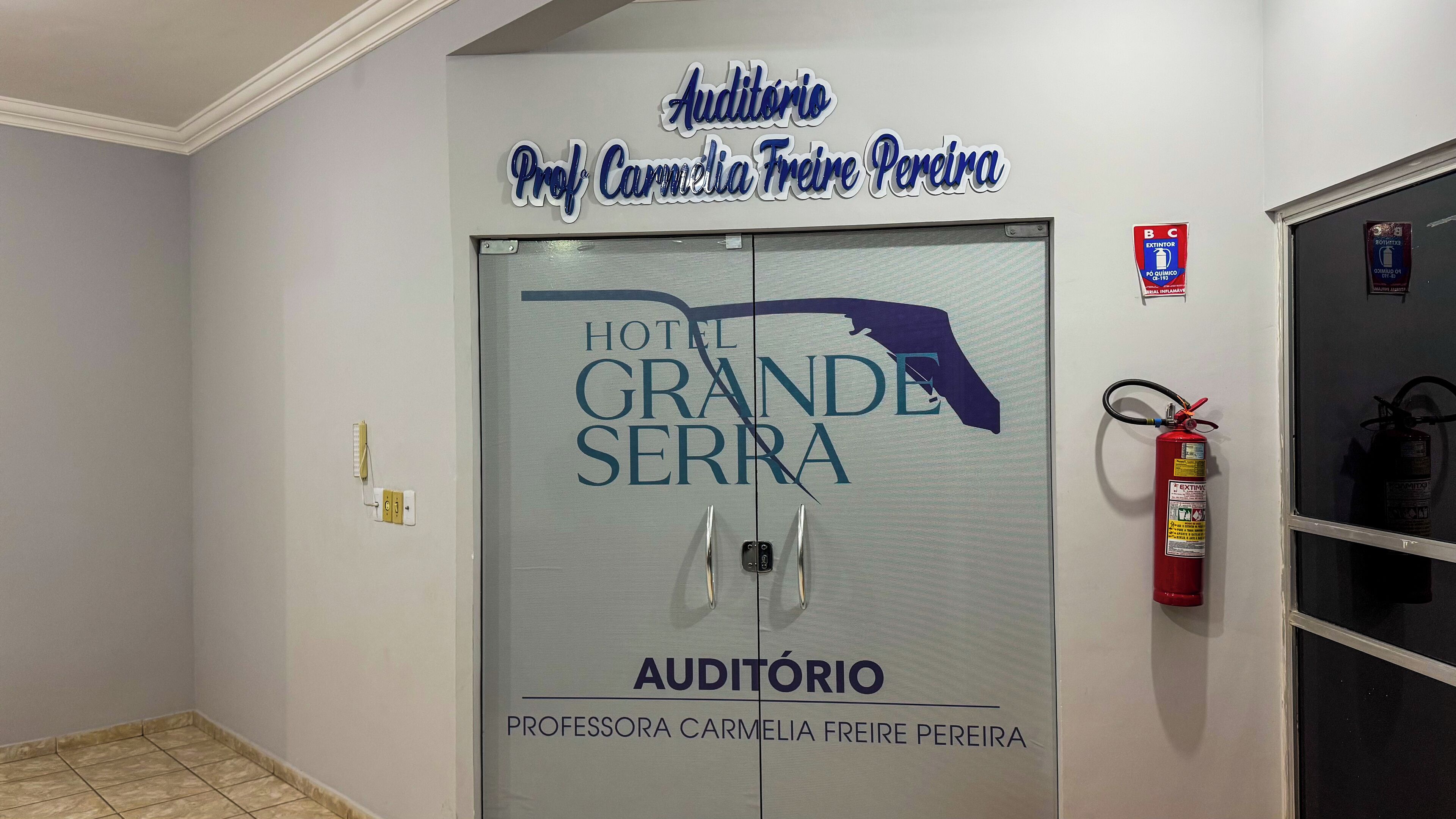 A hotel entrance with a sign reading "Auditorio Professora Carmelia Freire Pereira" and "Hotel Grande Serra."
