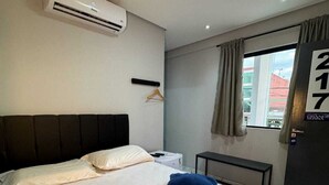 Habitación de hotel con dos camas, aire acondicionado, ventana con cortinas y vistas a un edificio.