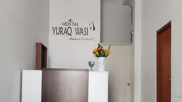 Un comptoir d’accueil avec une enseigne indiquant « HOSTAL YURAQ WASI » et une plante en pot posée sur le comptoir.
