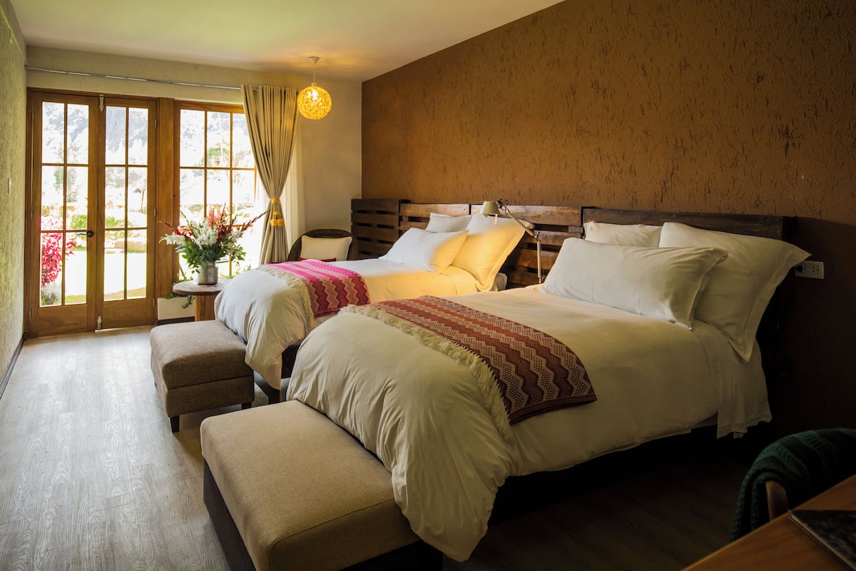 A bedroom with a large bed, a bedside table, a lamp, and a window with curtains.
