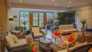 A spacious living room with wicker furniture, a glass coffee table, and a view of the garden through large windows. - Lamay Lodge by Mountain Lodges of Peru (Lamay)