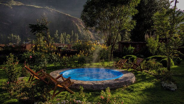 A hot tub surrounded by lush greenery and wooden chairs, set in a garden with flowering plants and a mountainous backdrop. - Lamay Lodge by Mountain Lodges of Peru (Lamay)