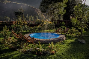 A hot tub surrounded by lush greenery and wooden chairs, set in a garden with flowering plants and a mountainous backdrop. - Lamay Lodge by Mountain Lodges of Peru (Lamay)