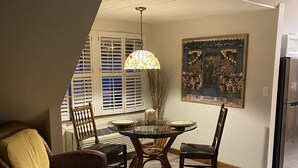 Un comedor con una mesa y sillas de vidrio, una lámpara colgante y un cuadro en la pared.