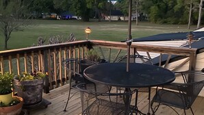 Una terraza de madera con una mesa redonda y sillas, un paraguas y plantas en macetas.