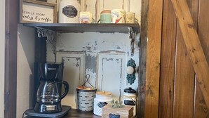 Un rincón rústico para café con cafetera, frascos y un cartel que dice 'Coffee is more unless it's coffee'.