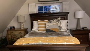 Un dormitorio con cama de madera, ventilador de techo, ventana con contraventanas y un cuadro de aves colgado en la pared.