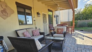 An outdoor patio with wicker furniture, including a sofa and chairs, a glass table, and a ceiling fan. - Breathtaking views in Tucson - Relax and refresh in a peaceful neighborhood.  (Tucson)