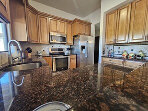 A kitchen with granite countertops, stainless steel appliances, wooden cabinets, and a stainless steel sink. - Breathtaking views in Tucson - Relax and refresh in a peaceful neighborhood. (Tucson)