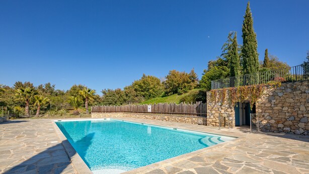 A rectangular swimming pool with stone tiles, surrounded by a stone wall and a wooden fence.