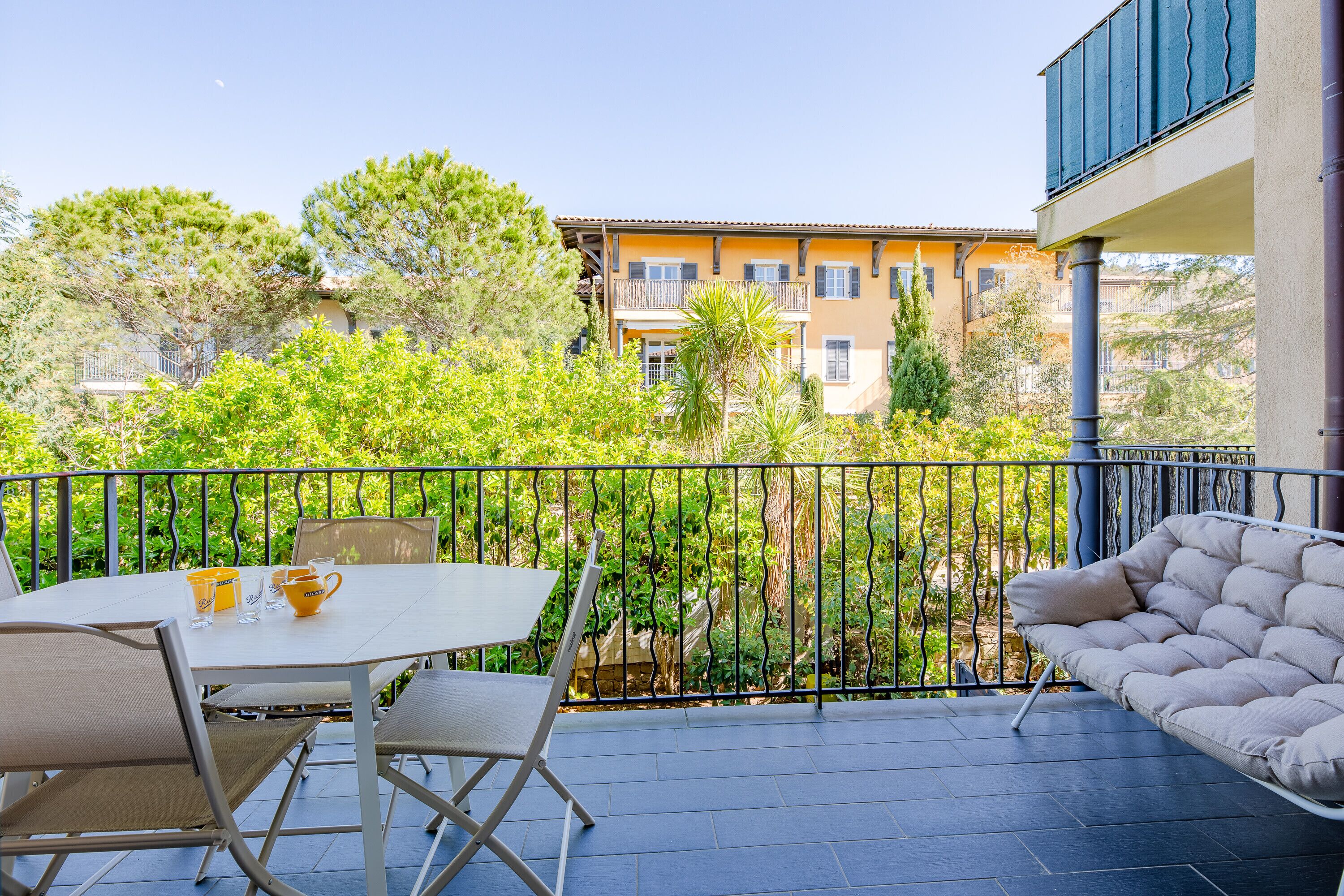 A balcony with a table and chairs, a sofa, and a view of a building and trees.