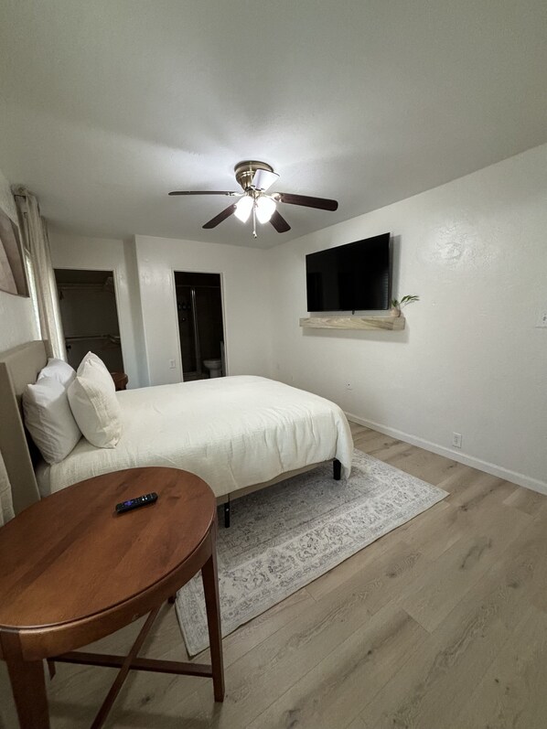 A bedroom with a bed, a ceiling fan, a TV mounted on the wall, and a wooden table.