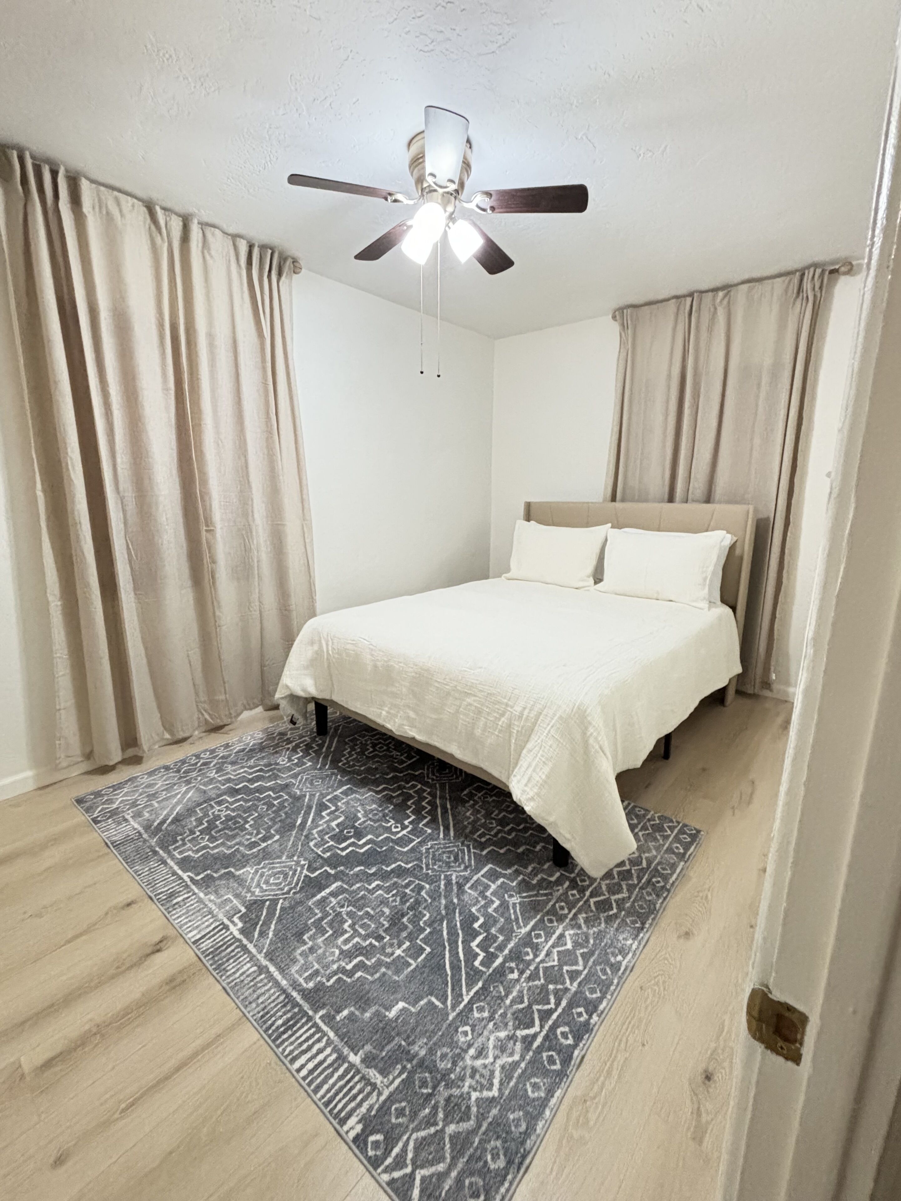 Un dormitorio con una cama, un ventilador de techo y una alfombra estampada.