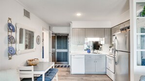 A modern kitchen with white cabinetry, a stainless steel refrigerator, and a dining area with a white table and bench. - Atlantic Beach Condo w/ Balcony & Beach Access! (Atlantic Beach)