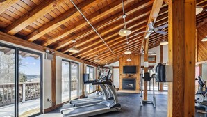 Un gimnasio espacioso con cinta de correr, ventiladores de techo y chimenea.