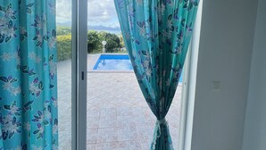 A room with a sliding glass door leading to a patio with a swimming pool. - Te Tai Marama (Raiatea)