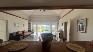 A spacious living area with a dining table, sofas, and a view of the outdoors. - Te Tai Marama (Raiatea)