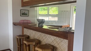A kitchen with a woven partition, a window with greenery outside, and three bamboo stools. - Te Tai Marama (Raiatea)