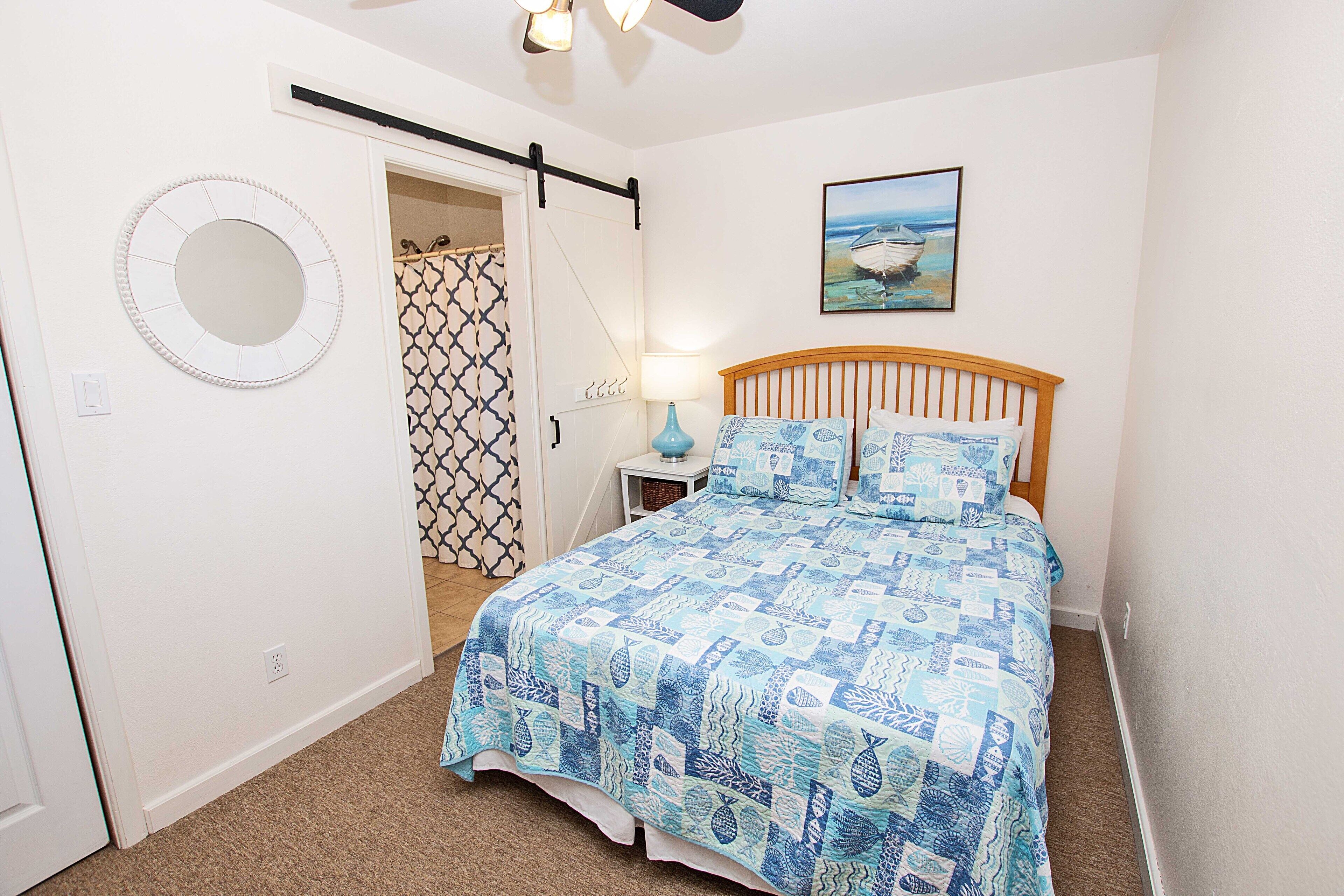 Une chambre à coucher avec un lit, une table de chevet, une lampe, un miroir rond, une porte et un tableau accroché au mur.