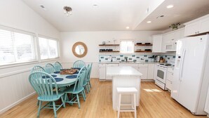 Una cocina moderna con armarios blancos, una isla central y un comedor con sillas turquesa.