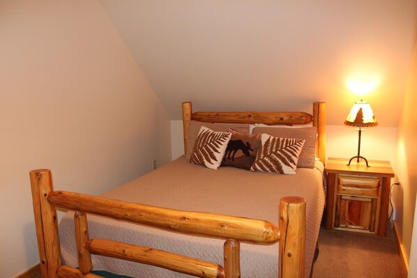 Een houten bed met hoofdeinde, een nachtkastje met lamp en decoratieve kussens.