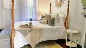 A bedroom with a four-poster bed, a bedside table, a mirror, and a window with curtains. - Walk to Downtown Monroe- The Blue Daisy Cottage (Monroe)